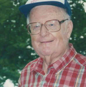 An older gentleman wearing glasses and a baseball cap smiles at the camera.