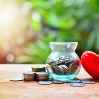 A jar of coins sits on the table next to a red heart.
