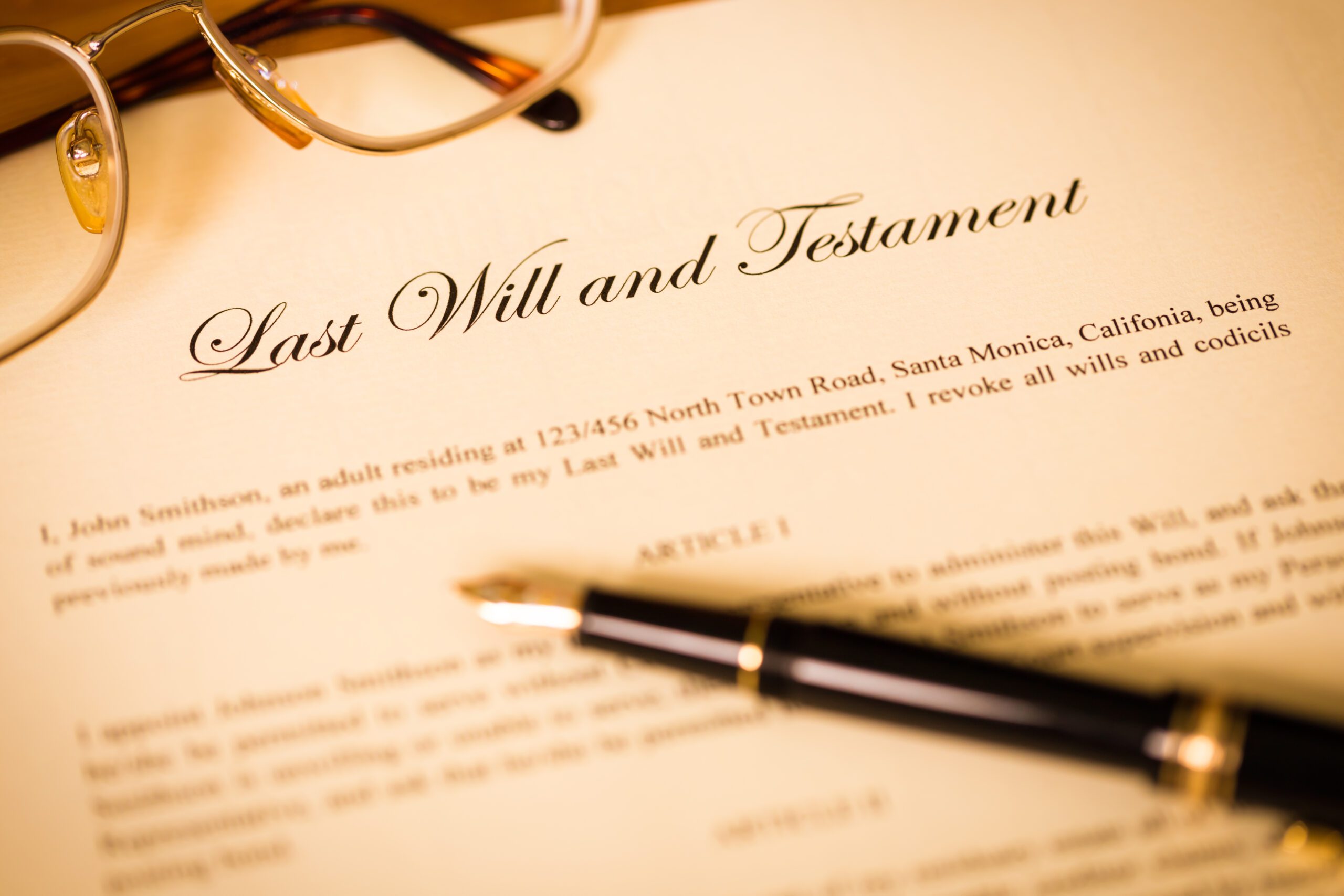 A document titled "Last Will and Testament" sits on a table with reading glasses and a pen.