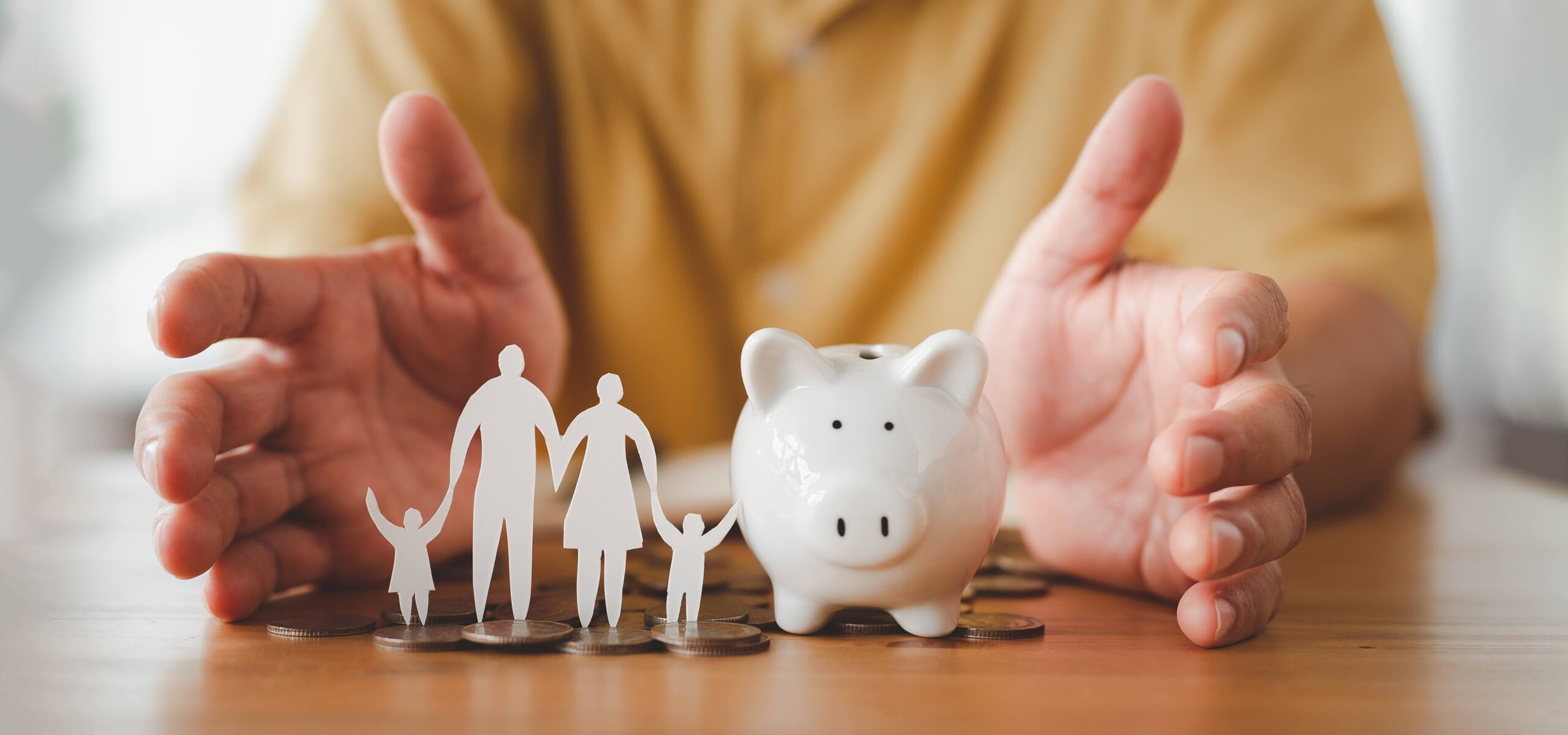 Hands form around a piggy bank next to a cutout of a family and coins. 