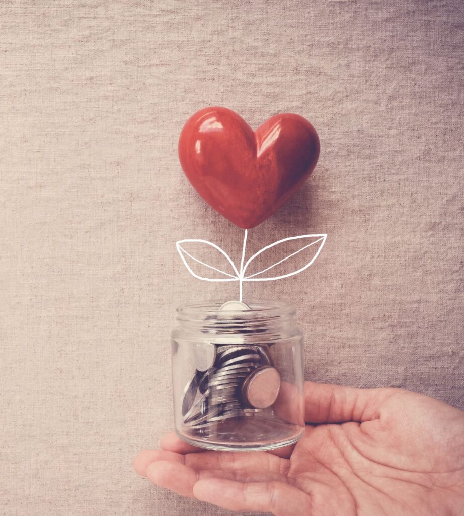 A hand holds a jar with coins in it and a heart growing out of the top.