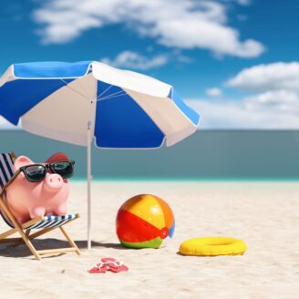 A piggy bank sits on the beach under an umbrella.