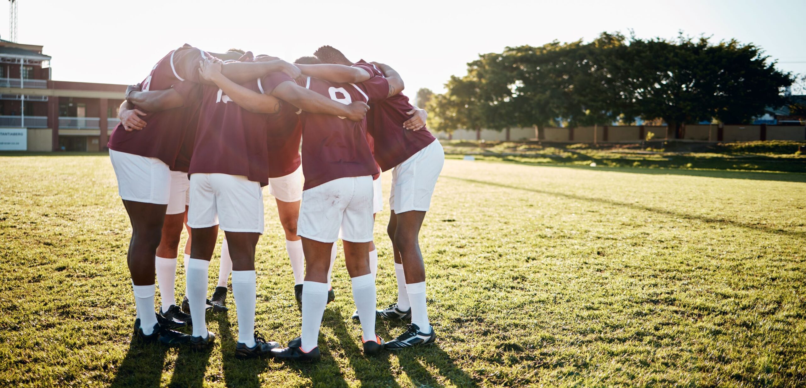 A group of men huddle on a sports field. 