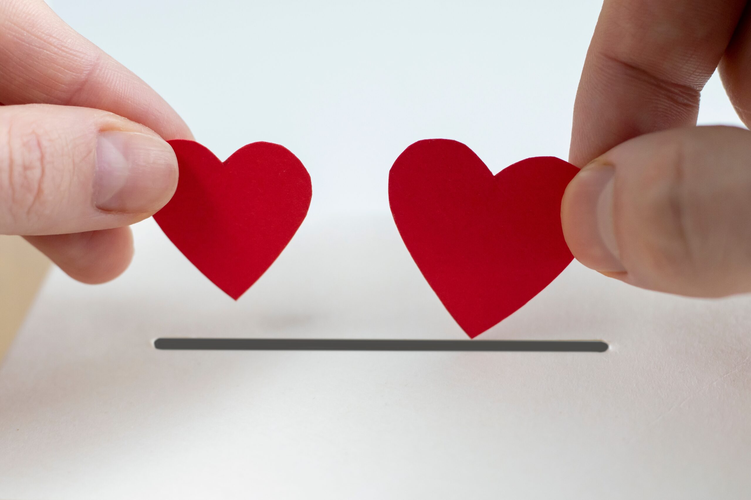 two hands drop small cut out paper hearts into a donation box opening