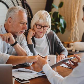 Older couple looks over paper work while younger man holds a tablet device for them to review