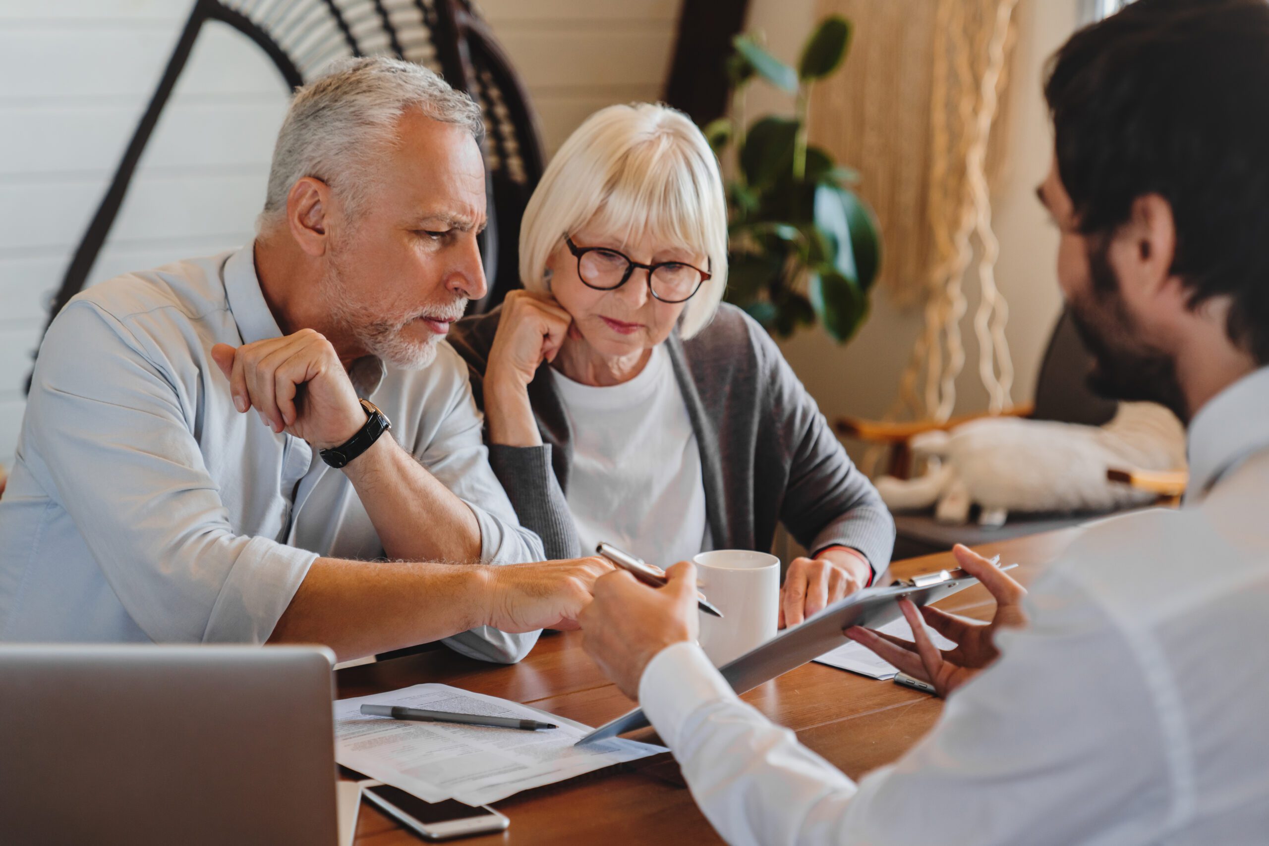 Older couple looks over paper work while younger man holds a tablet device for them to review