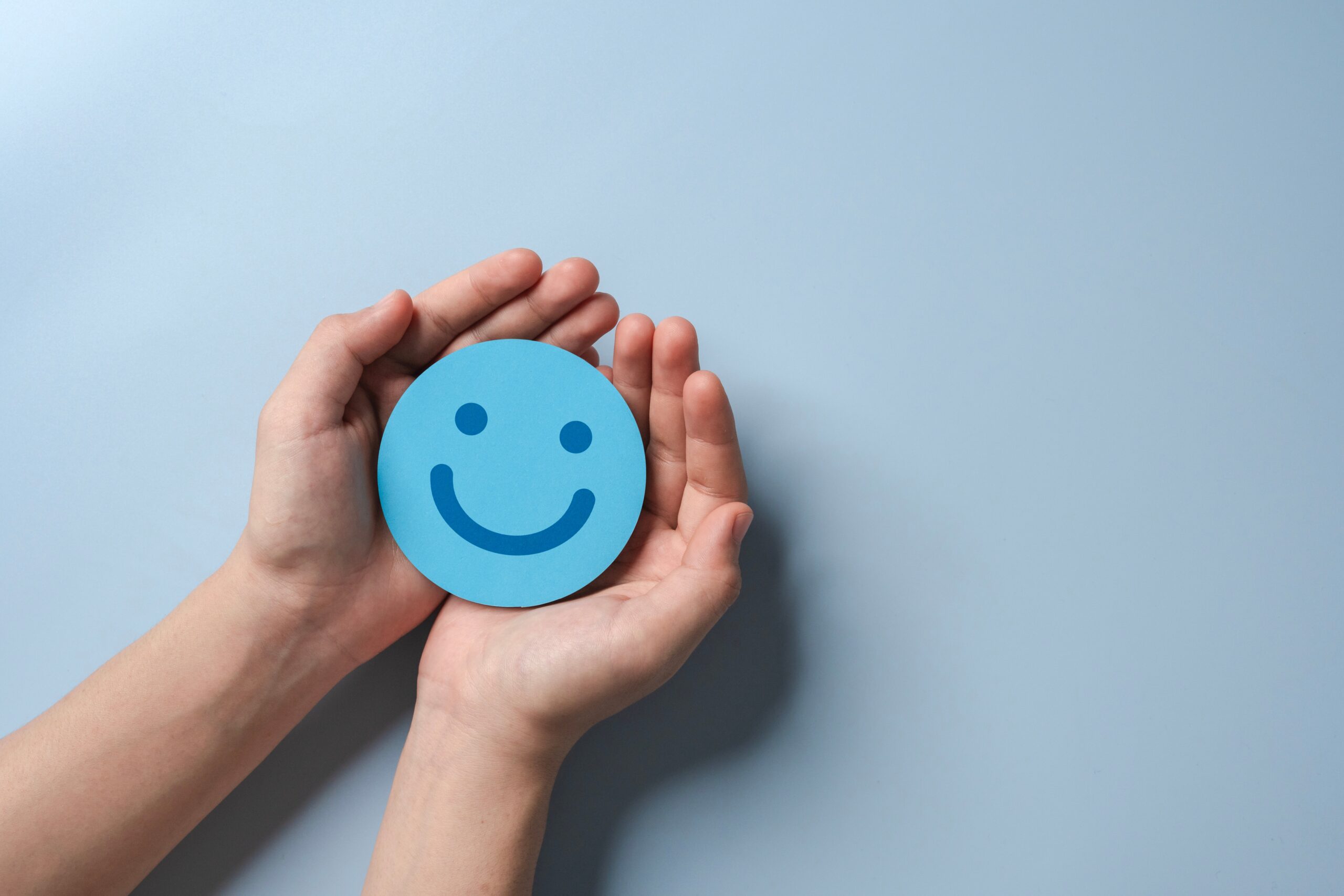 blue paper smiley face held out in open hands on a white background