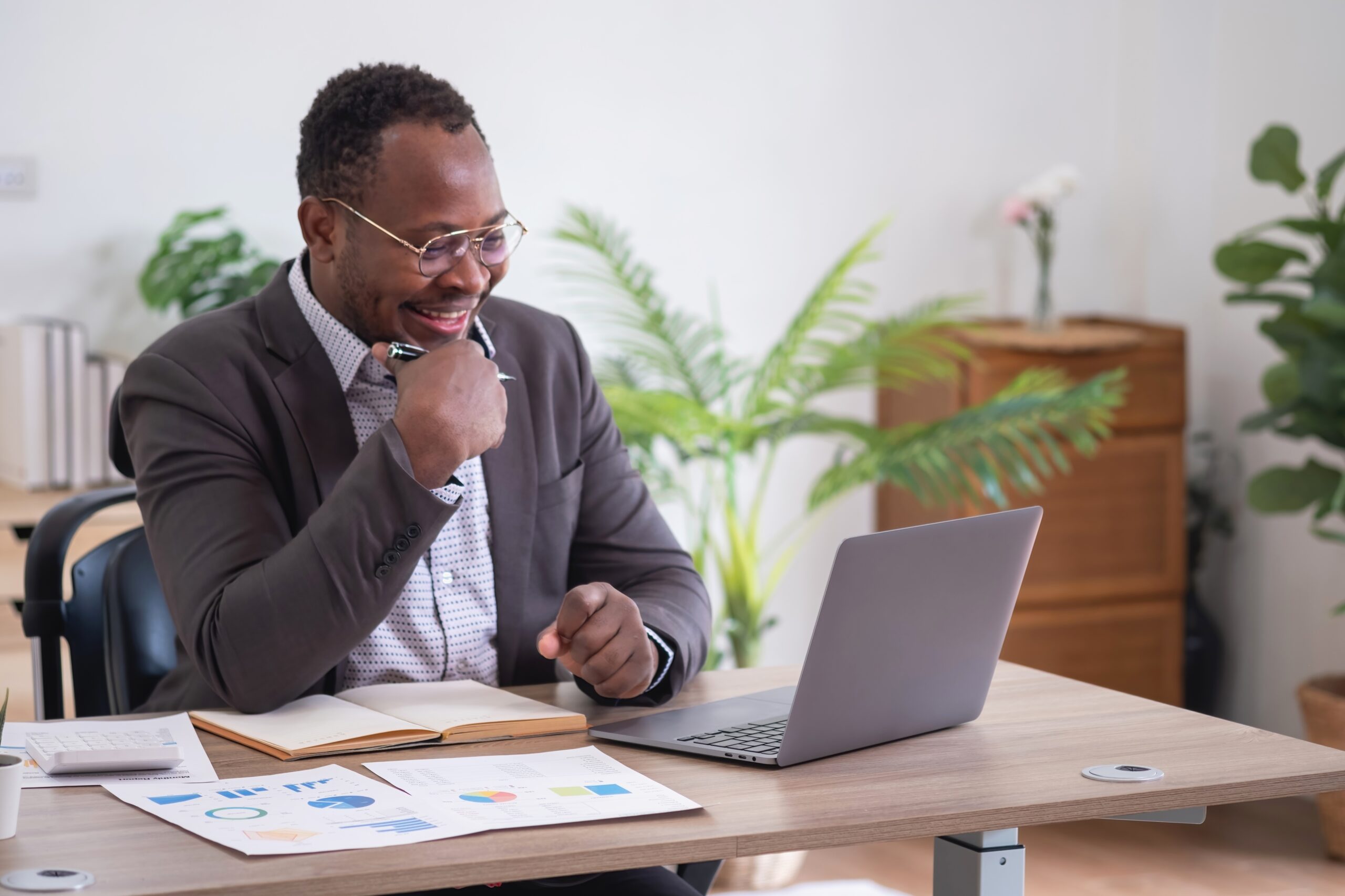 African American Businessman sits at a laptop laughing with paperwork on the table in front of him