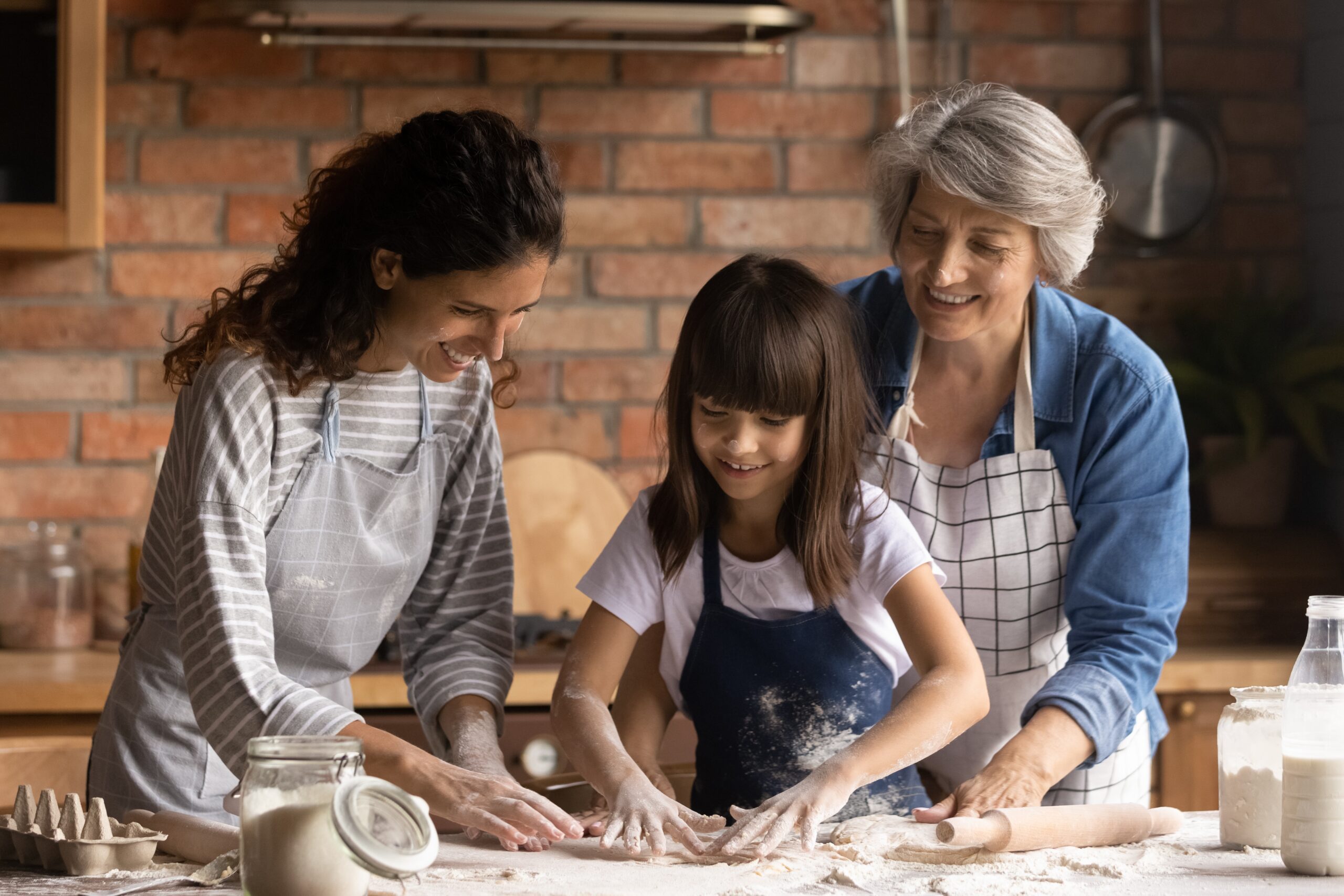 Three women are baking in a kitchen. An adult, a child, and a mature woman are baking together