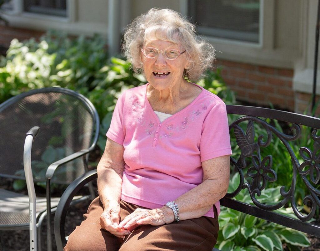 older woman sitting on a bench in the sunshine smiling