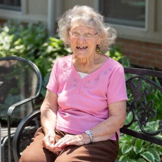 older woman sitting on a bench in the sunshine smiling