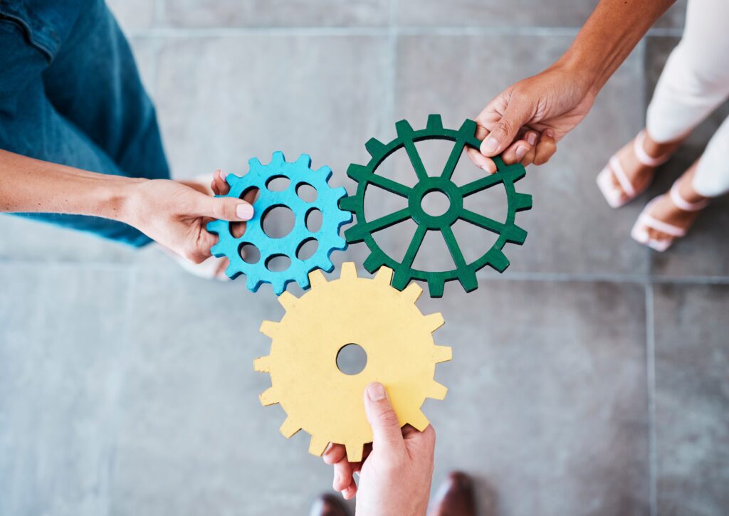 Three hands holding gears of blue, green, and yellow. 