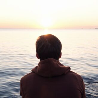 Man sits on the waters edge at sunset