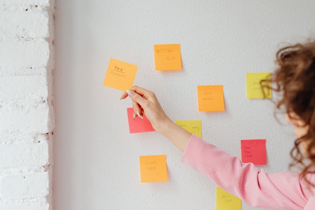 multi-colored sticky notes on a wall with various financial terms on them. A woman's hand is picking one up to read