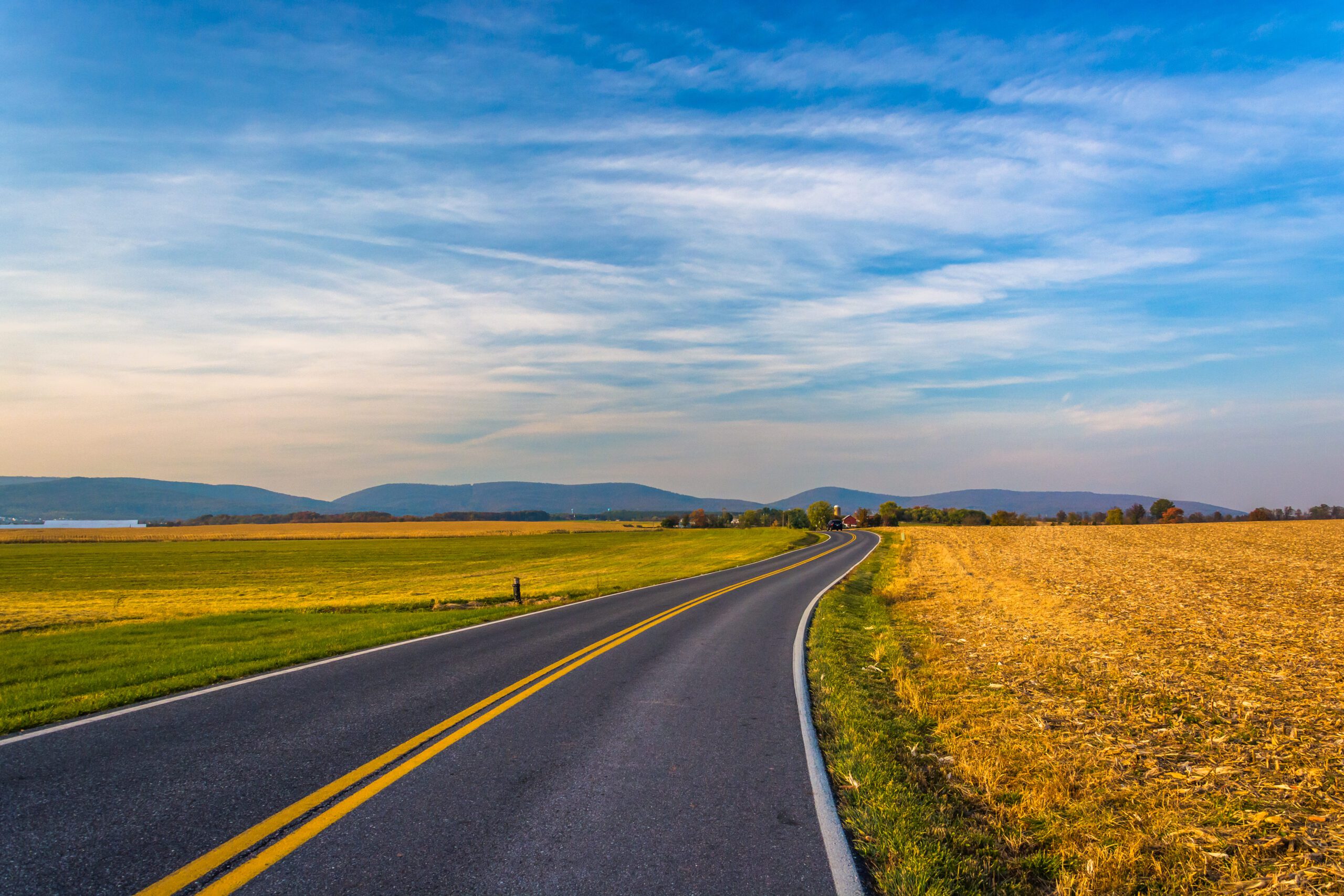 A two lane road lined with fields going off towards mountains