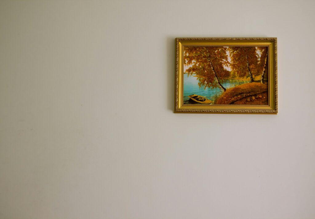 a framed piece of art featuring a scenic landscape hangs on a white wall in a golden frame