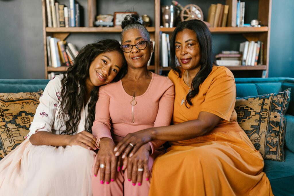three generations of women sit on a couch together holding each other and smiling at the camera